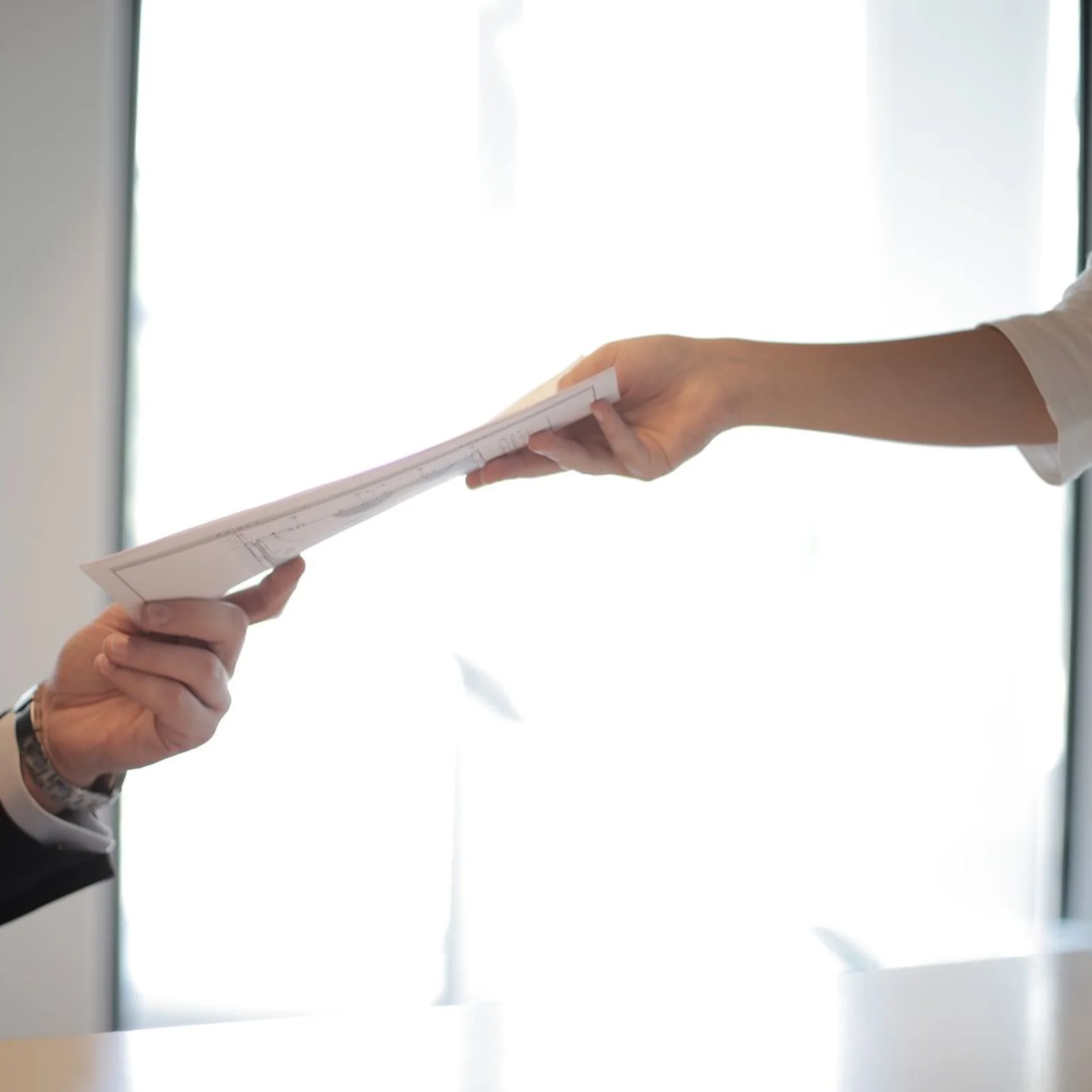 Two hands passing a document across a desk.