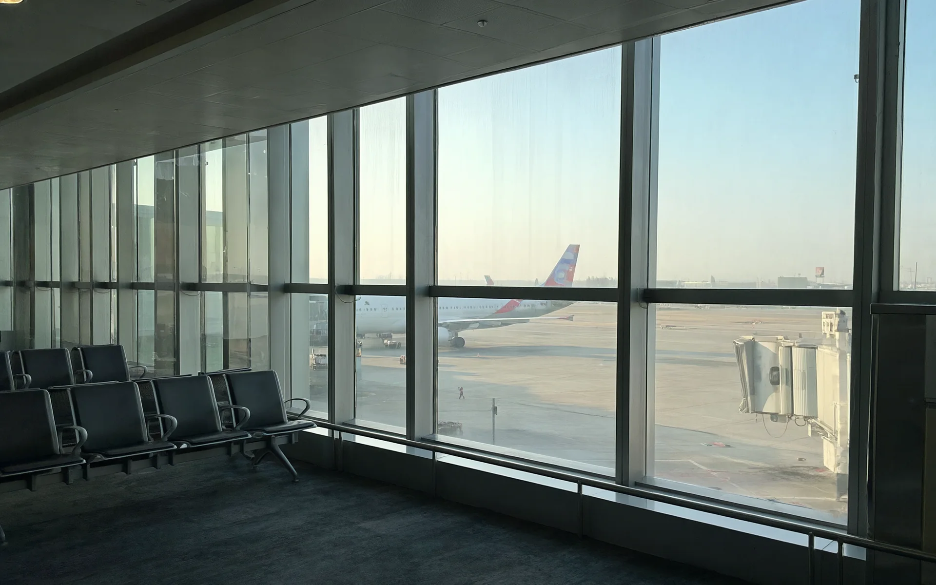 An airport departure hall with glass walls and a parked aircraft outside.